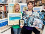 Cindy Hagen And Jake Grzech Holding Some Of Their Paintings With Others Displayed Around Them