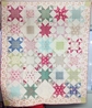 Quilt With Pastel And Primary Colored Stars Pattern On A White Background With A Floral Edging, "Strawberry Fields" By Leslie Horoshko